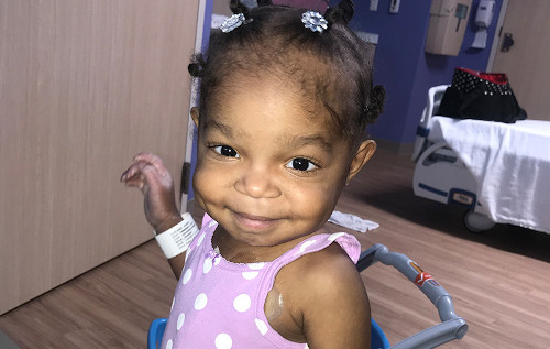 波士顿儿童医院的病人Khori身穿粉红色的圆角棉布连衣裙，微笑着