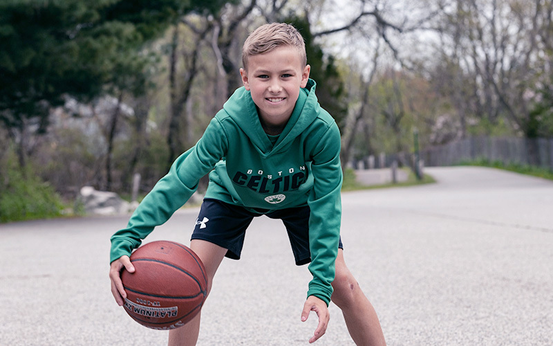 穿着波士顿凯尔特人绿色运动衫的男孩在马路上运球