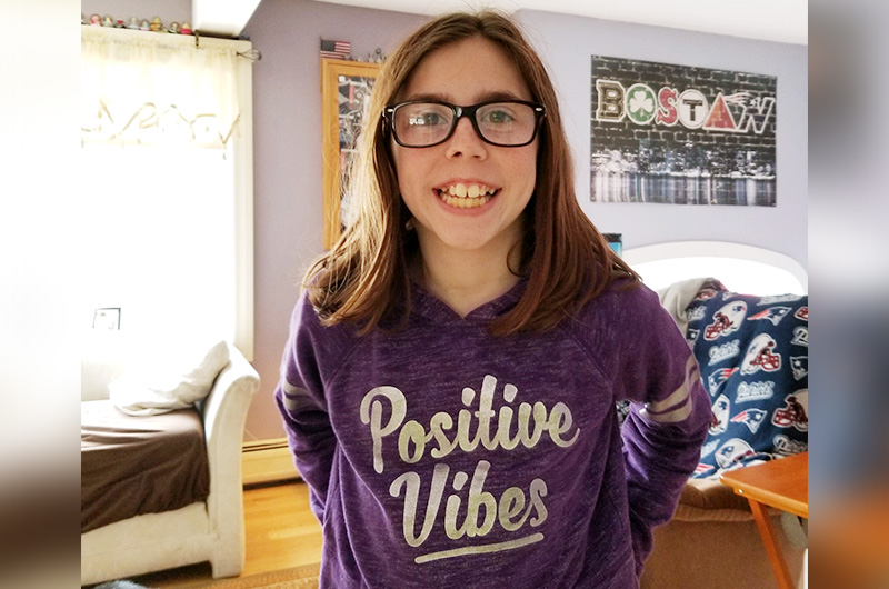 戴着眼镜，穿着紫色t恤的年轻女孩站在卧室里。
