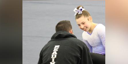 Mikayla参加体操比赛后，与教练交谈并微笑。